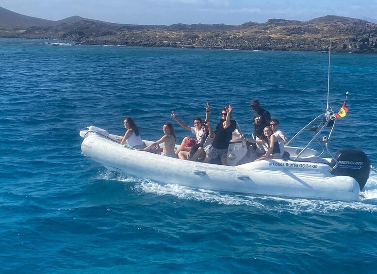 A group of people on a small inflatable boat in the ocean with a mountainous coastline in the background. 4