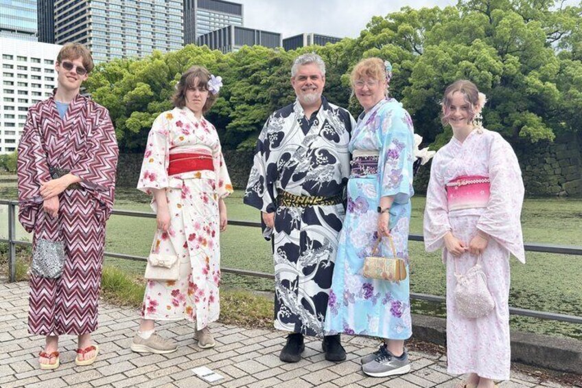 Four people in traditional Japanese kimonos standing on a paved walkway with a park and buildings in the background. 3