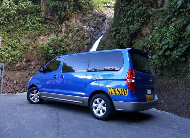 A blue van with 'TURISMO' on the side parked by a cliff with a waterfall. 2