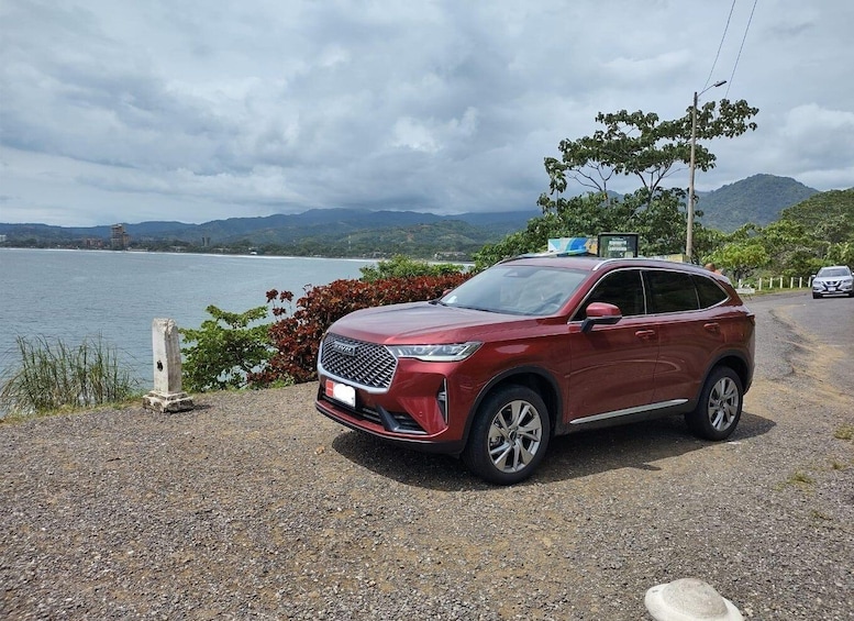 A red SUV parked by a lakeside with mountains in the background. 1