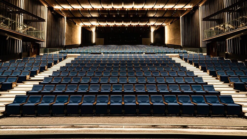 Ein großes, leeres Auditorium mit Reihen blauer Sitze und einer Bühne im vorderen Bereich. 5