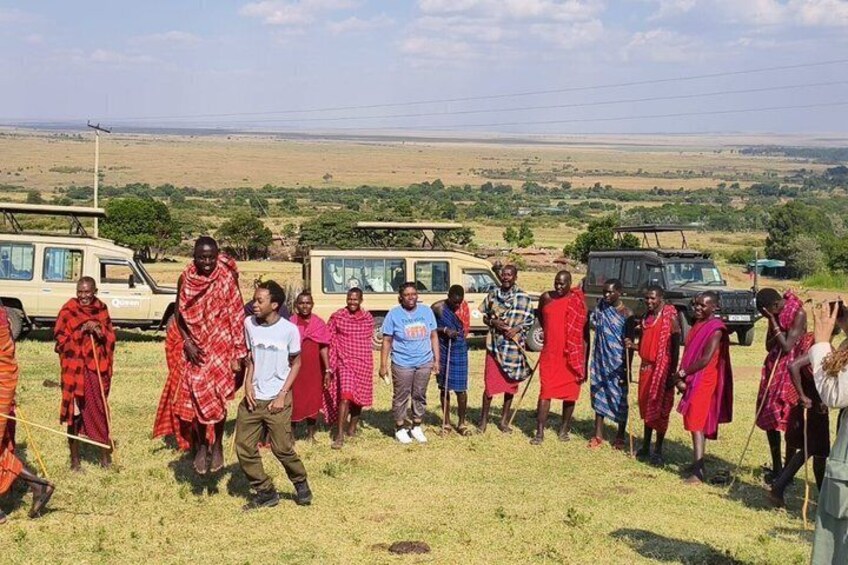 A group of people standing in a grassy field with vehicles in the background. 2