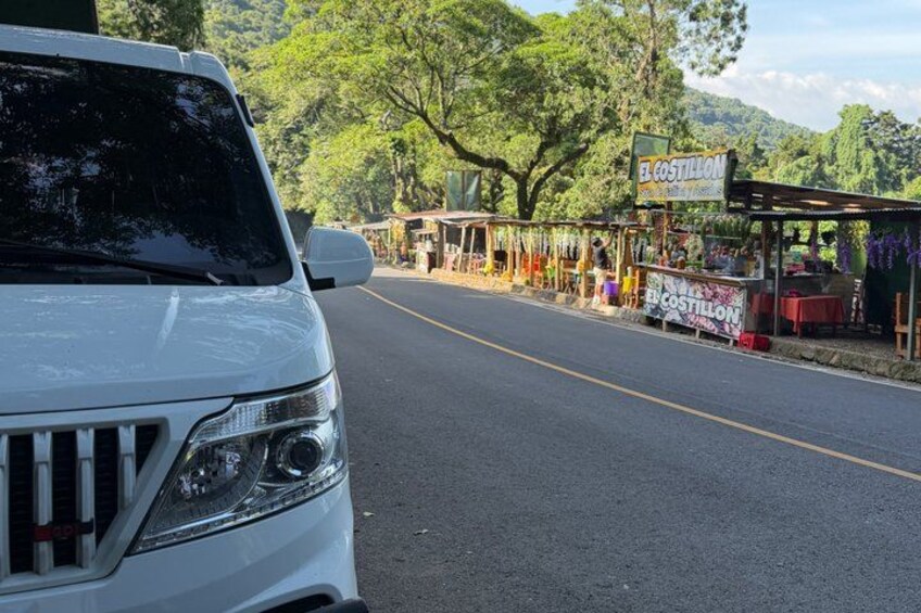 A white SUV parked on a road with a roadside stand named 'El Costillón' in the background. 3