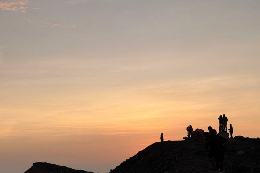A sunset over a mountainous landscape with people standing on a hill. 1