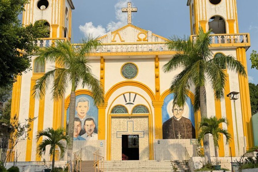 A church with yellow and white exterior, palm trees, and murals of religious figures. 4