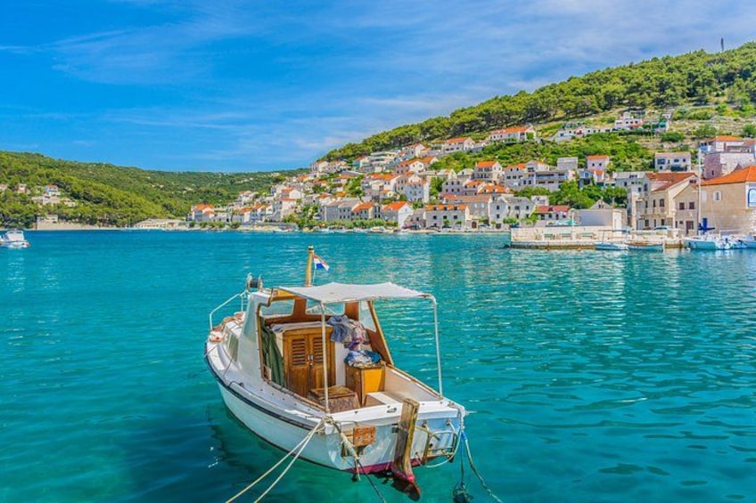 A boat anchored in clear turquoise waters with a coastal village in the background. 1