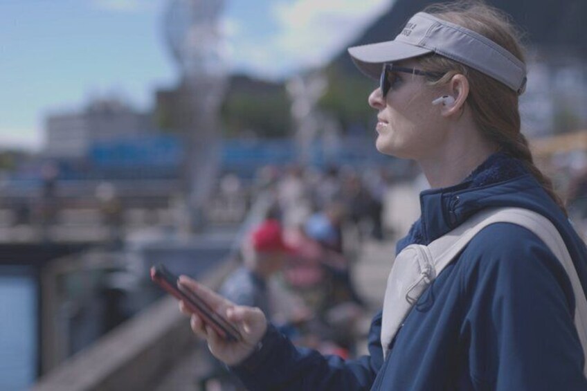 A person standing by a body of water, holding a smartphone. 1