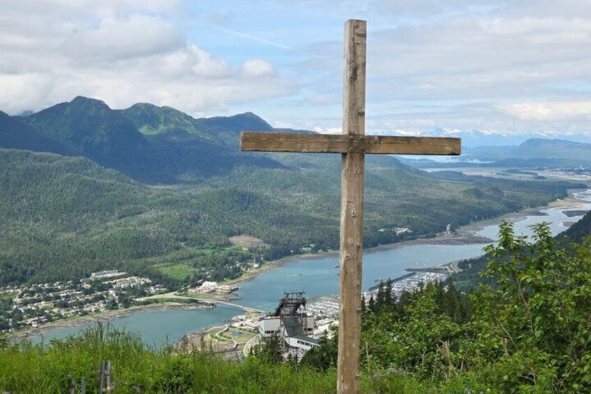 A wooden cross, a river, mountains, and a town in the background. 3