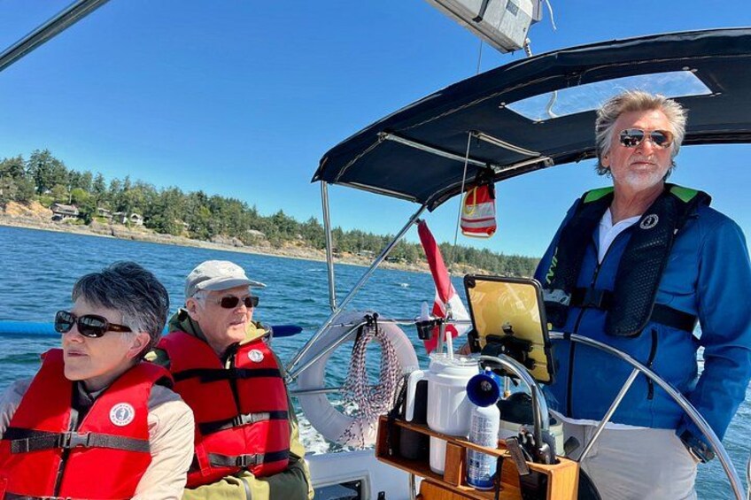 Three people on a sailboat with life jackets, a fan, and a water bottle on deck. 2
