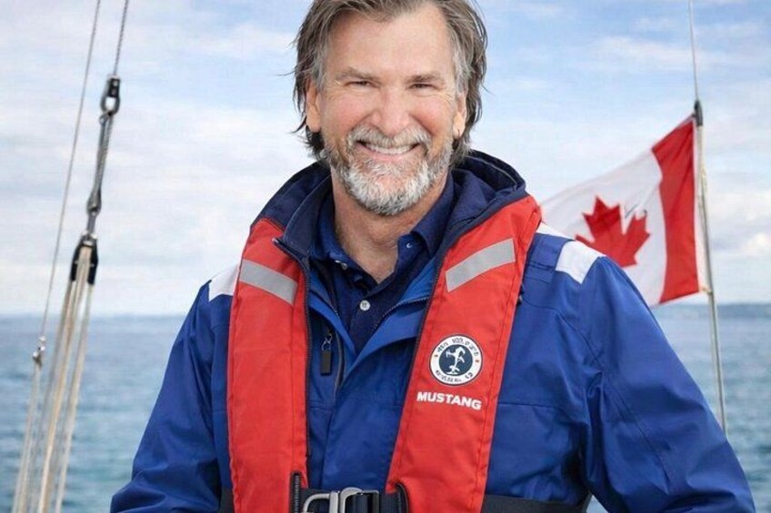 A person wearing a blue jacket with a red life jacket and a Canadian flag in the background. 1
