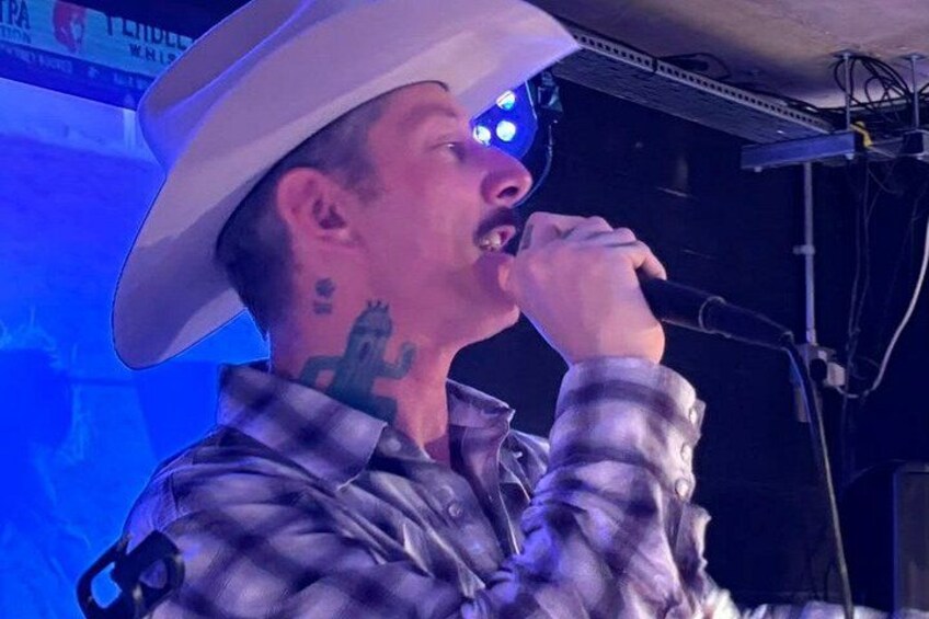 A person with a cowboy hat and a plaid shirt, holding a microphone. 3