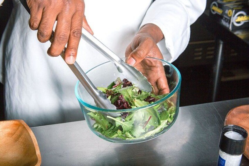 A person mixing salad in a glass bowl. 5