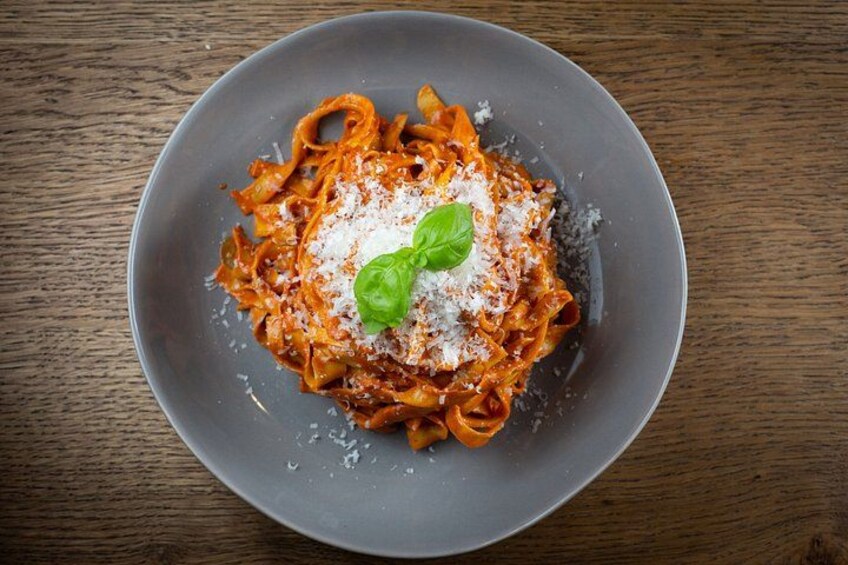 A plate of pasta with tomato sauce, grated cheese, and a basil leaf on a wooden table. 3