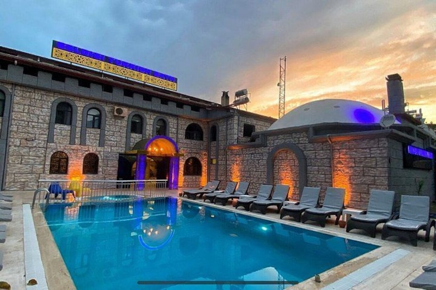 A swimming pool with lounge chairs, a stone building with arches, and a sunset sky. 1