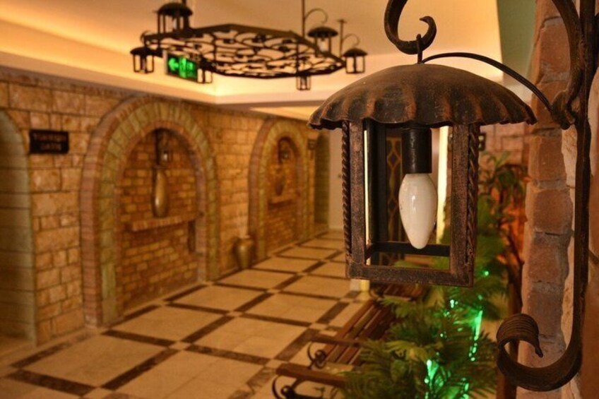 A corridor with stone walls, a tiled floor, and a hanging lantern. 5