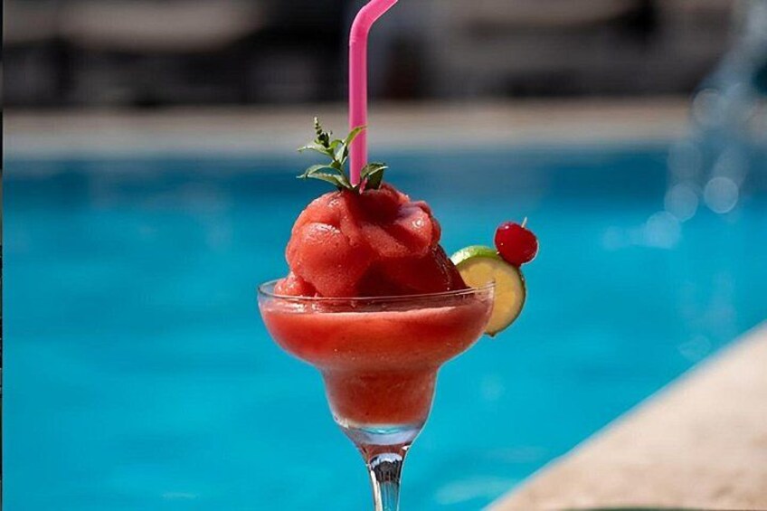 A cocktail with a pink straw, garnished with a cherry and a slice of lime, next to a pool. 4