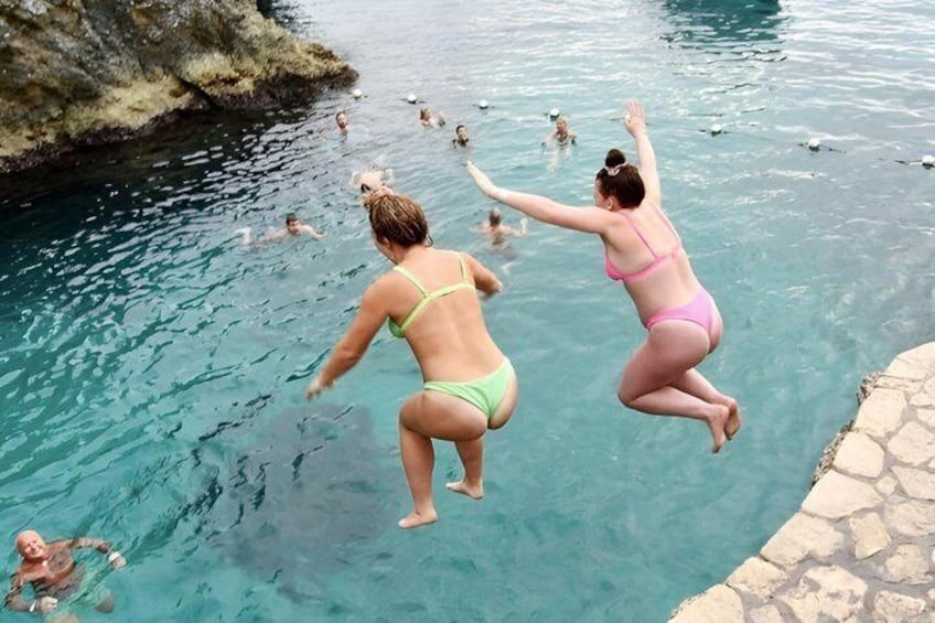 People jumping into a clear blue pool with rocky formations nearby. 5