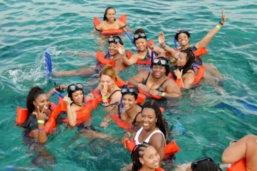 A group of people in a clear blue body of water, wearing life jackets and snorkels. 1