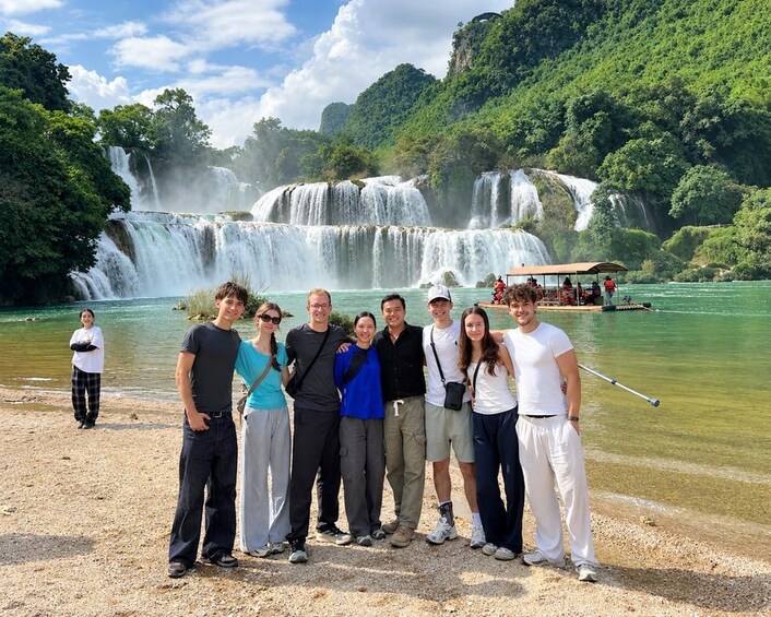 A group of people standing on a beach with a waterfall in the background. 1