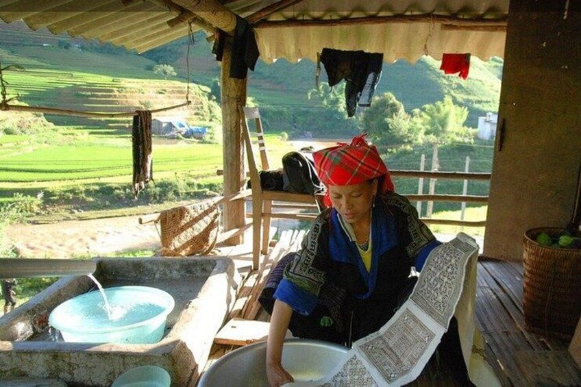 A person reading a book in a rustic outdoor setting with a wooden structure, a water basin, and a view of green fields. 4