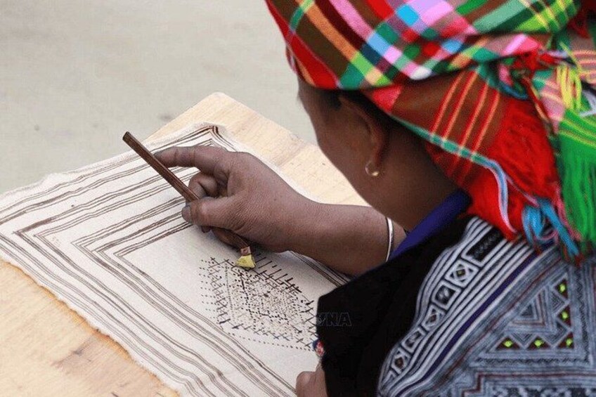 A person drawing on a patterned cloth with a stick. 3