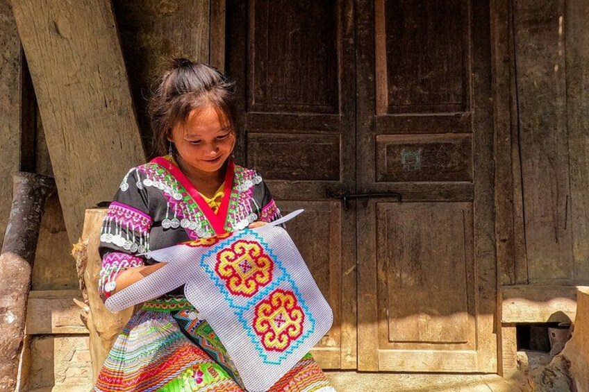 A person sitting on a wooden bench, holding a piece of colorful fabric with a geometric pattern. 5