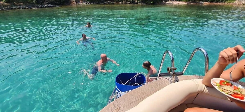 A boat with people swimming in the water, a dock, and a clear blue sky. 1