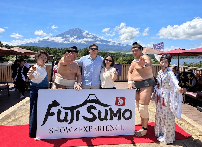 A group of people posing with a sign that reads 'Fuji Sumo Show Experience' in front of a mountain. 3