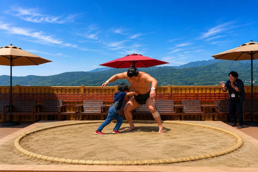 A sumo wrestling match on a sandy stage with mountains in the background. 2