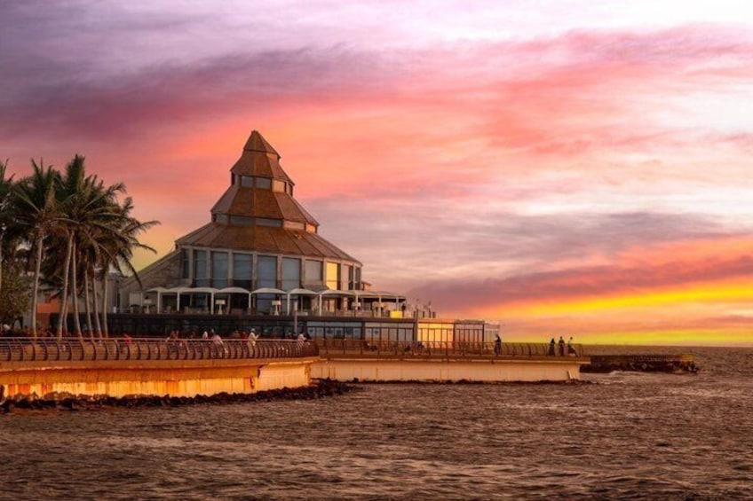 A coastal building with a unique pyramid-like roof, palm trees, and a sunset. 5