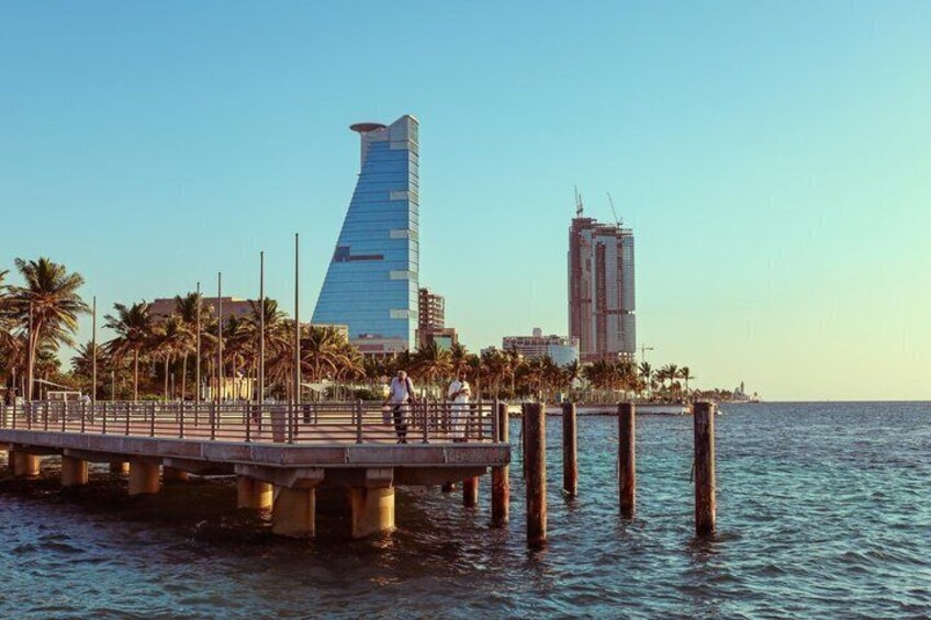 A waterfront promenade with palm trees, a modern glass building, and a pier extending into the water. 3