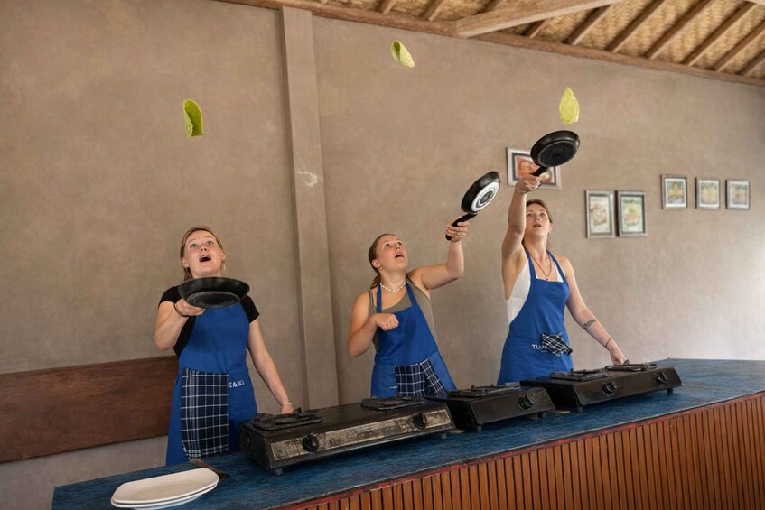 Three people in blue aprons performing a juggling act with frying pans. 1