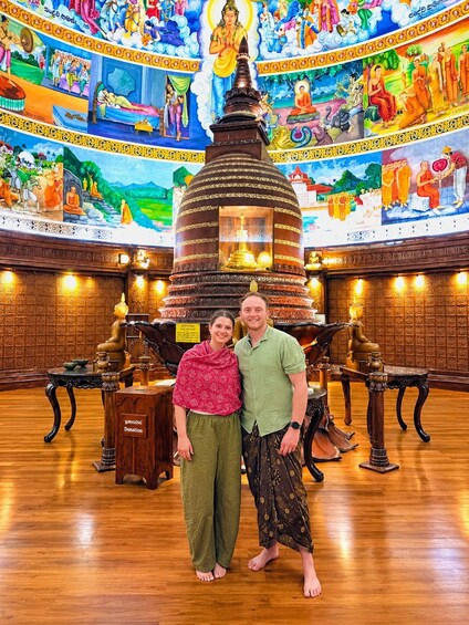 A temple interior with a large stupa, intricate murals, and two people standing in front. 2