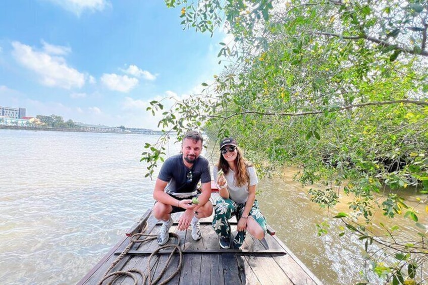 Two people on a wooden boat near a riverbank with trees. 5