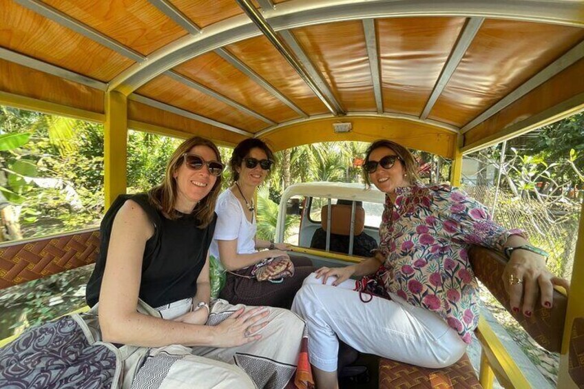 Three people seated in a covered vehicle with a wooden roof, surrounded by greenery. 4