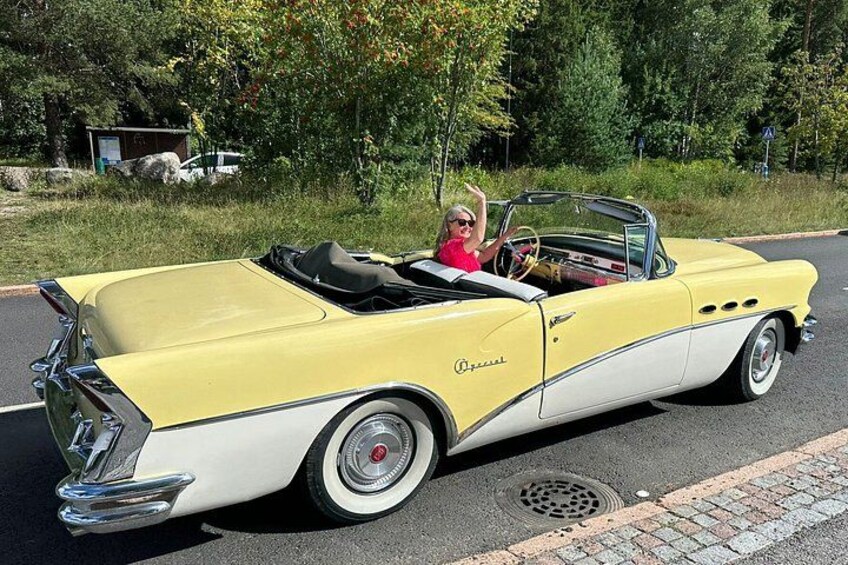 A vintage yellow convertible car with a woman driving and another person in the passenger seat. 2