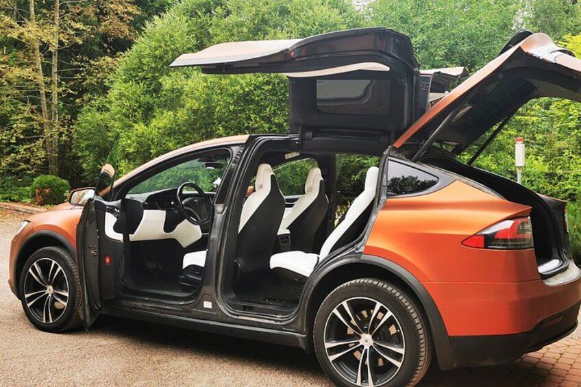 A convertible car with its top down, parked on a paved surface with greenery in the background. 3
