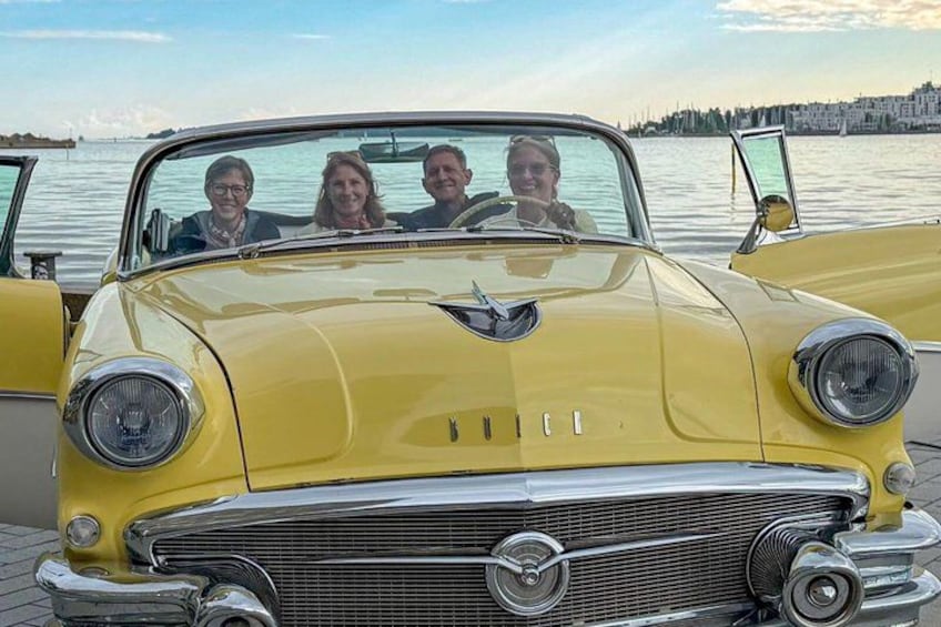 A yellow vintage car with four people seated in the front. 3