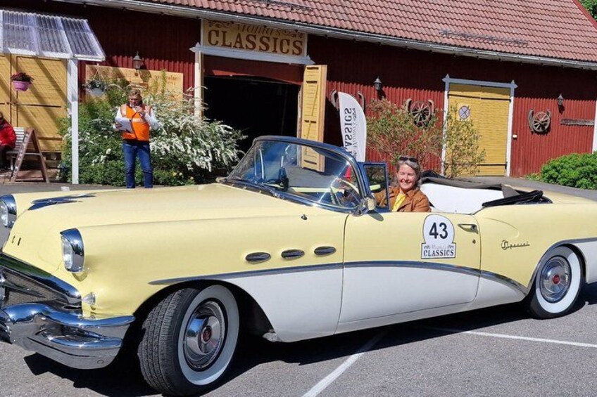 A vintage yellow convertible car with the number 43 parked in front of a building with a red roof. 2