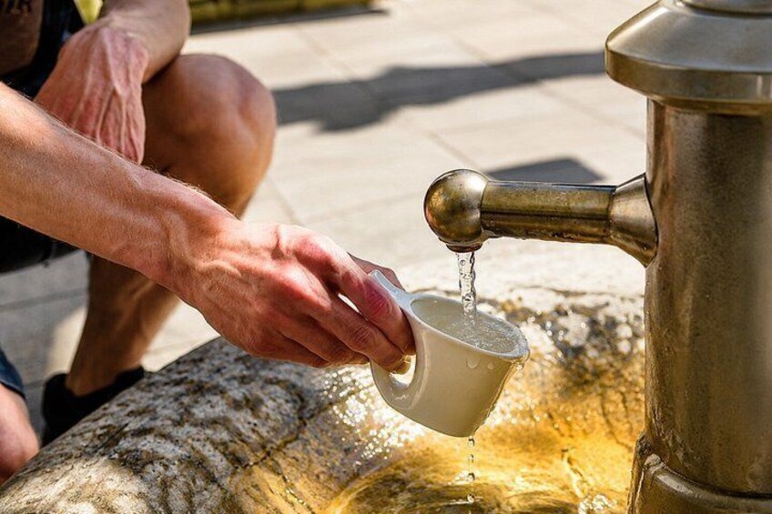 A person filling a cup with water from a metal tap. 5
