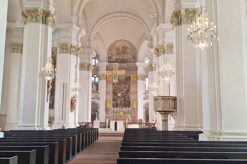 An interior of a church with rows of pews, ornate chandeliers, and a large altar. 2