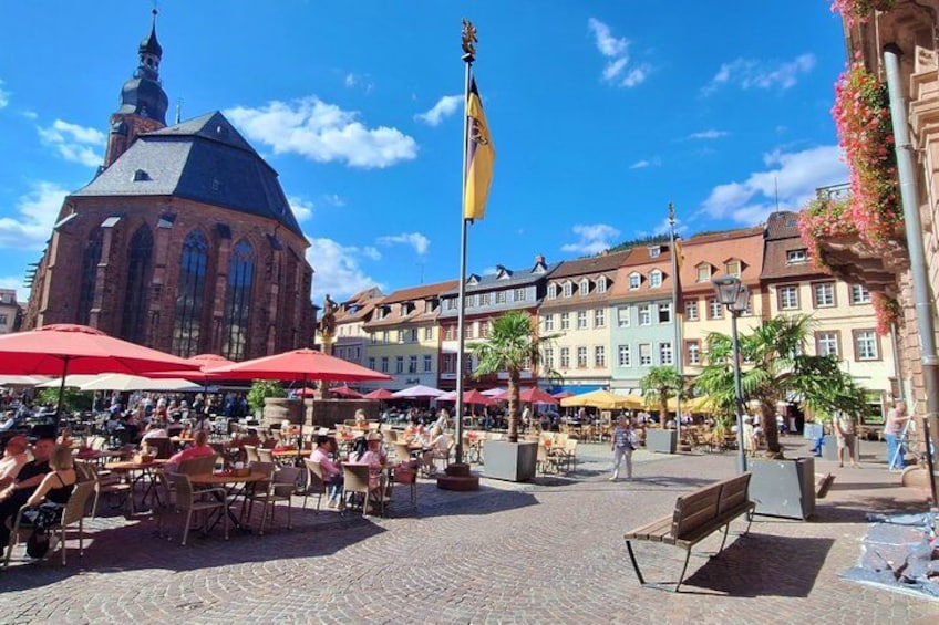 A cobblestone square with outdoor seating, a historic building with a dome, and a flagpole. 1