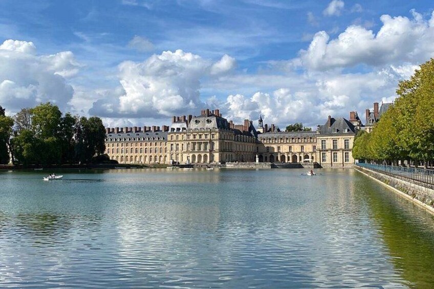 A river with a historic building on the left and a tree-lined path on the right. 1
