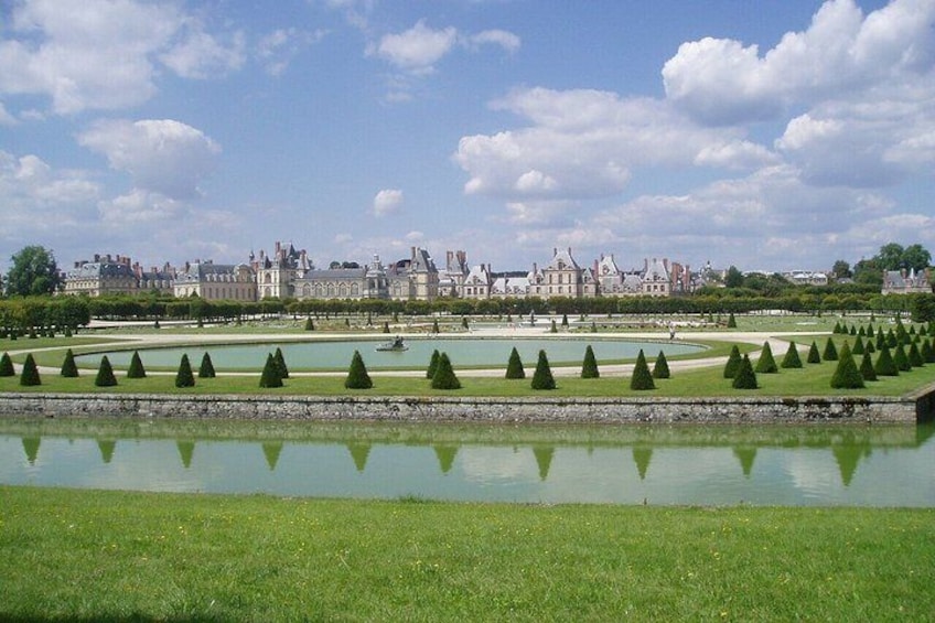 A formal garden with a water feature, neatly trimmed hedges, and a distant view of a historic building complex. 4