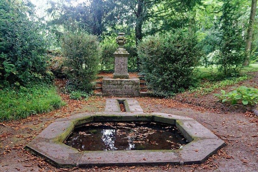 A stone fountain surrounded by lush greenery and a stone monument in a forested area. 3