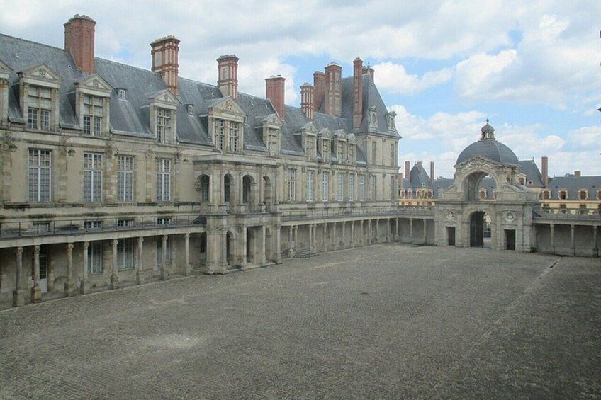 A historic courtyard with a large building featuring multiple chimneys and a dome structure. 5