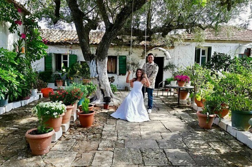 A courtyard with potted plants, a white building with green shutters, and a person in a white dress. 4