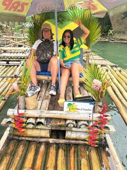 Two people on a bamboo raft with a sign for Ellis Tours & Transfers. 5
