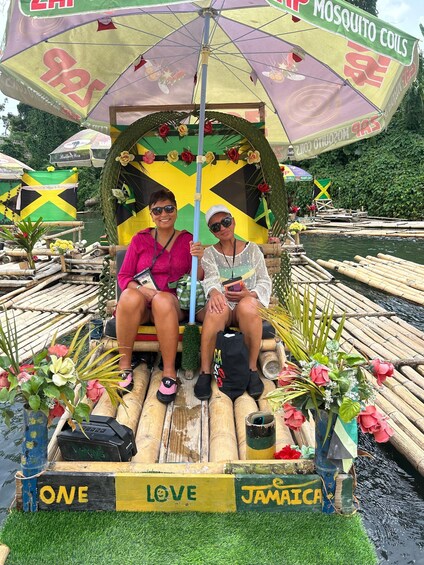 Two people seated on a decorative float with a sign reading 'ONE LOVE' and 'JAMAICA' in front. 2