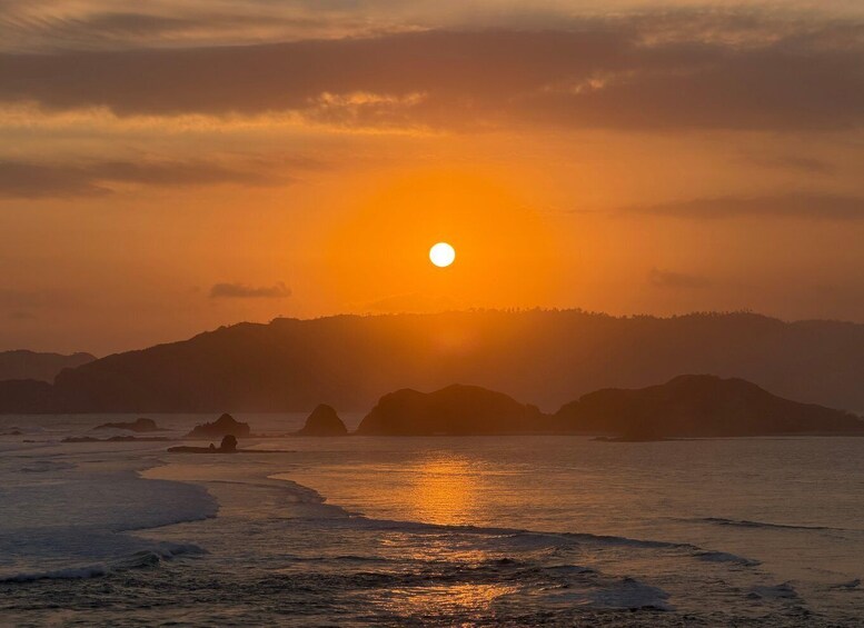 A sunset over a coastal landscape with mountains in the background and waves on the shore. 3